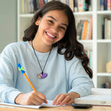 Young adult female smiles while wearing dark purple fox chew necklace. She is writing using a Munchables Toolbox Fidget Pencil Topper Stim