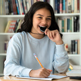 Teenager girl chewing oreo anxiety necklace in black. Holding chewable pencil topper.