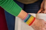Adult wears all 7 rainbow coloured Munchables Stretchy Coil Fidget Bracelets