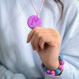 Girls hand holding purple outline butterfly chewelry and wearing sensory bracelet