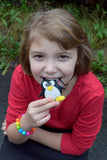 Munchables Penguin Chew Necklace being chewed on by girl. Doesn't picture beads that come standard.