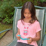 Girl playing with Squishy Caterpillar Stim Toy. She is wearing a pink Munchables Owl Pendant Chew Necklace.