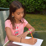 Girl sitting writing with a pencil with a Munchables Toolbox Pencil Topper spinner fidget toy on it.
