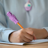 Girl writes with pencil that has purple robot chewy pencil topper on it.